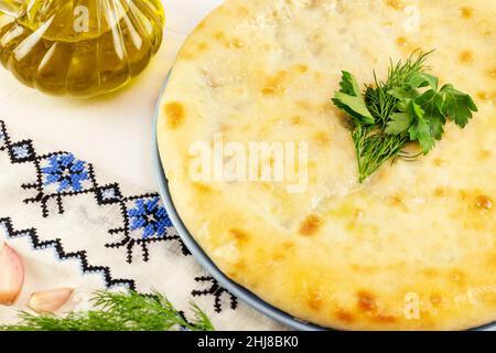 Una torta Ossezia fatta in casa con spinaci, olio d'oliva, prezzemolo, aneto e aglio su sfondo bianco. Composizione alimentare nazionale con pi Foto Stock