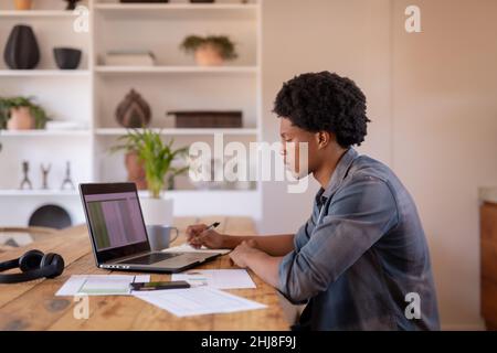 Vista laterale della scrittura afro-americana del giovane imprenditore mentre usando il laptop al tavolo. Inalterato, commercio, tecnologia senza fili, lettura, concentrazione, Foto Stock