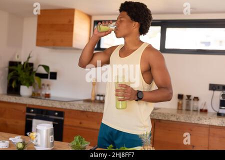 Frullato afro-americano bevendo frullato mentre si trova in cucina a casa. Inalterato, influencer, bevanda sana, vita biologica e sana Foto Stock