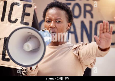 La forza è ciò di cui abbiamo bisogno. Scatto di una giovane donna con la mano sollevata parlando attraverso un megafono per una protesta. Foto Stock