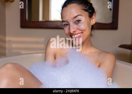 Ritratto di bella ragazza sorridente biraciale in vasca da bagno saponata al centro benessere. Inalterato, spa, cura del corpo, stile di vita, sensualità, vitiligo e benessere. Foto Stock