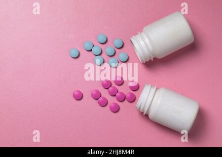 Pillole blu e rosa di medicinali o vitamine fuoriescono da vasi bianchi su sfondo rosa Foto Stock