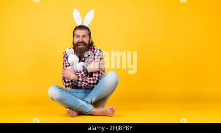 l'uomo bearded divertente indossa le orecchie del coniglietto. il ragazzo in costume del coniglio che si diverte. festa di festa di primavera. caccia alle uova. l'uomo felice brutale su sfondo giallo Foto Stock