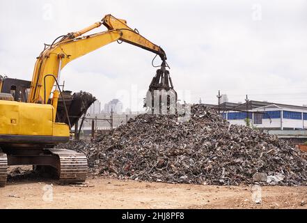 Appena un altro giorno nello scrapyard. Scatto ritagliato di un escavatore che smista attraverso una pila di rottami metallici. Foto Stock