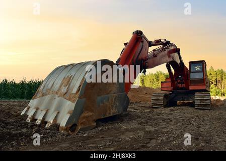 Scavatore scavo trincea su sfondo tramonto. Backgoe su lavori di terra. Costruzione del gasdotto naturale. Costruzione del liquame e drenaggio. Fognatura di posa Foto Stock
