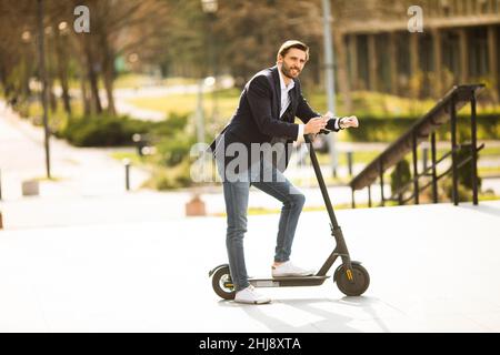 Bel giovane uomo d'affari che usa il telefono cellulare su scooter elettrico Foto Stock