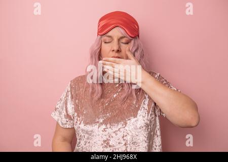 La donna addormentata vuole dormire, sentendosi esausta, sbadigliata, coprendo la bocca con la mano, svegliarsi presto isolato su sfondo rosa. Foto Stock