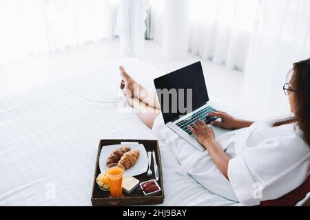 Donna irriconoscibile che scrive sul laptop che si agghiacciano sul letto Foto Stock