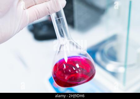 Matraccio rotondo con un campione di sangue negli scienziati, in un laboratorio moderno con bilancia analitica sullo sfondo, indossare guanti di gomma. Foto Stock