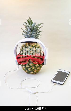 Ananas con bicchieri da discoteca, cuffie bianche e smartphone. Concetto di festa tropicale. Foto Stock