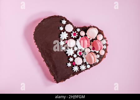 Vista dall'alto della torta a forma di cuore rosa con glassa al cioccolato, meringhe e amaretti sulla parte superiore come decorazione. San Valentino, giorno delle madri. Foto Stock