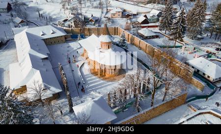 Fotografia aerea del monastero di Voronet, situato nella contea di Suceava, in Romania in inverno, giorno di sole con neve. La foto è stata scattata da un drone. Foto Stock