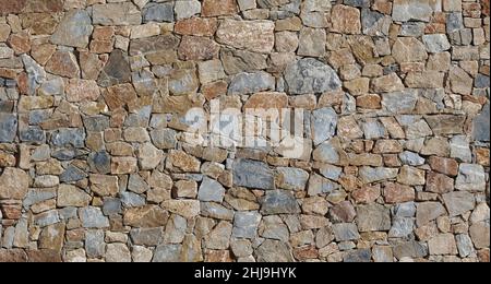Parete esterna rustica realizzata con pietre naturali piatte marroni di diverse dimensioni disposte a caso. Sfondo e trama Foto Stock