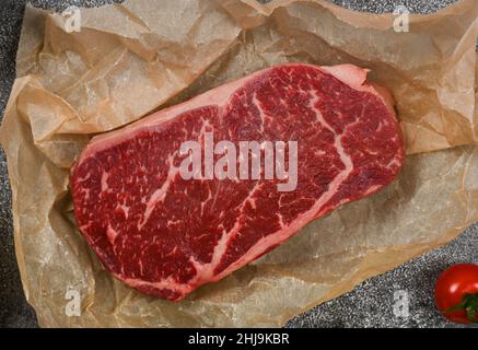 Primo piano su una prima bistecca di manzo marmorizzata cruda di sirloin su carta marrone pergamena che avvolge sul tavolo, vista dall'alto sopraelevata, direttamente sopra Foto Stock