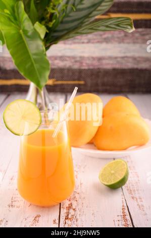 La foto mostra vetro trasparente con mango naturale martini. Sullo sfondo, esotici frutti di mango gialli possono essere visti. In primo piano sono presenti sezioni di citr Foto Stock