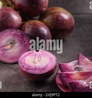 Foto mostra diversi frutti tropicali viola. Un frutto è tagliato aperto e l'interno è visibile. La frutta di Caimito è originaria della giungla del Repu Domenicano Foto Stock