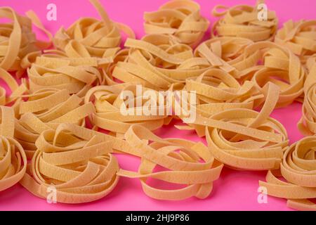 Tagliatelle crude , nidi di pasta, nidi di pasta all'uovo giacenti su un motivo su sfondo rosa, il motivo è una vista laterale dall'alto Foto Stock