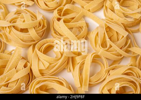 Tagliatelle crude , nidi di pasta, nidi di pasta all'uovo giacenti su un motivo su sfondo bianco, il motivo è una vista laterale dall'alto Foto Stock