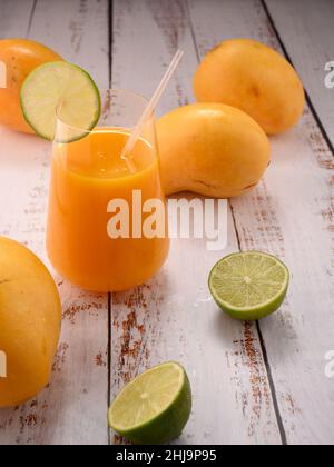 La foto mostra vetro trasparente con succo d'arancia fresco naturale su testurizzato vintage. Sullo sfondo, esotici frutti di mango gialli possono essere visti. In foregroun Foto Stock