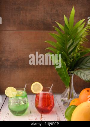 La foto mostra varietà di frutta fresca come mango, limoni, lime e arance. Al centro della foto sono 3 mocktails su tavola bianca in un vetro con una W. Foto Stock