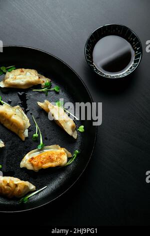 Adesivi tradizionali giapponesi gyoza pentola cotti in una padella in ghisa con olio e germogli verdi e posti sopra un moderno tavolo in legno nero. Foto Stock