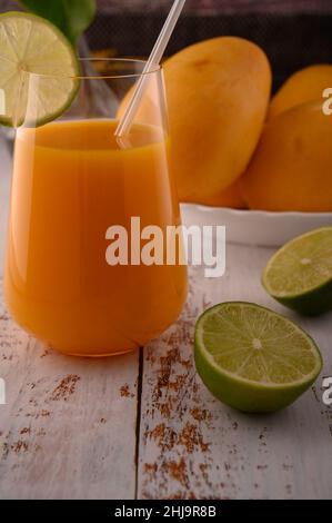 La foto mostra vetro trasparente con succo di carota fresco naturale su testurizzato vintage. Sullo sfondo, esotici frutti di mango gialli possono essere visti. In foregroun Foto Stock