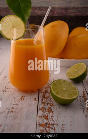 La foto mostra vetro trasparente con succo di mango fresco naturale su testurizzato vintage. Sullo sfondo, esotici frutti di mango gialli possono essere visti. In primo piano Foto Stock