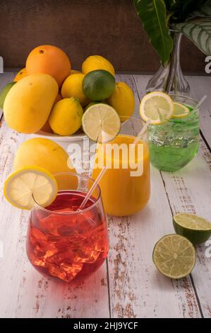 La foto mostra varietà di frutta fresca come mango, limoni, lime e arance. Al centro della foto sono 3 mocktails su tavola bianca in un vetro con una W. Foto Stock