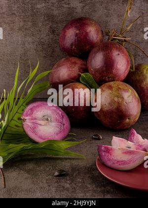 Foto mostra diversi frutti tropicali viola. Un frutto è tagliato aperto e l'interno è visibile. La frutta di Caimito è originaria della giungla del Repu Domenicano Foto Stock