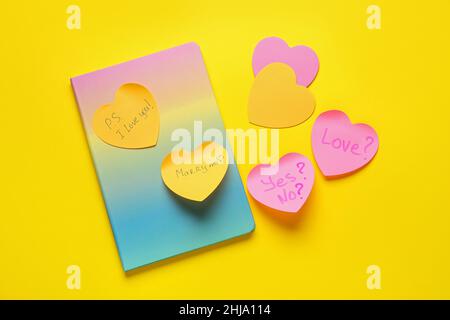 Note adesive a forma di cuore con parole e quaderno su sfondo giallo Foto Stock