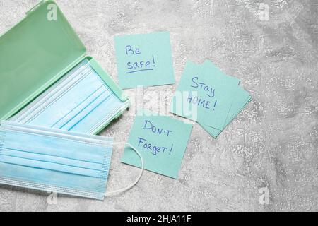 Maschere mediche, note adesive con testo STAY HOME, ESSERE AL SICURO e NON DIMENTICARE su grunge sfondo Foto Stock