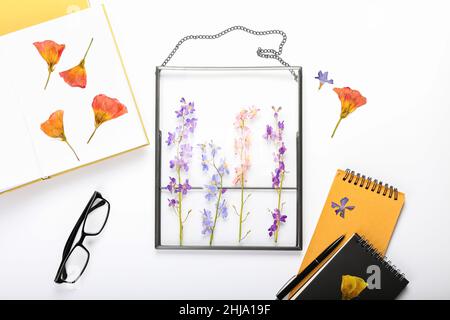 Composizione con fiori secchi pressati, libro, taccuino e occhiali su sfondo bianco Foto Stock