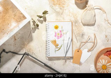 Composizione con fiori pressati secchi, taccuini e tessere bianche su sfondo chiaro Foto Stock