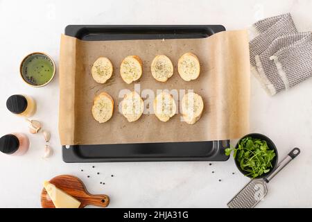 Foglio da forno con pezzetti di pane per preparare crostini e spezie su sfondo bianco Foto Stock