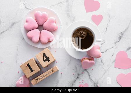 Calendario con data di San Valentino, tazza di caffè e gustosi macaroni a forma di cuore su sfondo chiaro Foto Stock