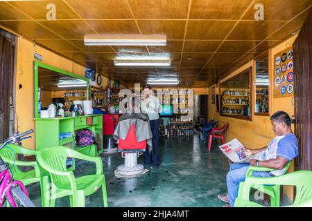 Il barbiere taglia i capelli di un uomo mentre un altro legge un giornale in un negozio di barbiere a Jinotega, Nicaragua Foto Stock