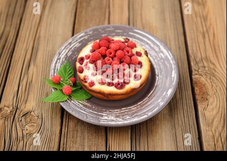 Torta yummy fatta in casa con lamponi selvatici freschi e foglie in piatto marrone su vecchio tavolo di legno copyspace orizzontale Foto Stock