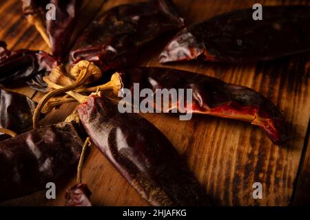 Cile Guajillo. Questo peperoncino messicano è la forma essiccata di peperoncino mirasol e viene utilizzato in una varietà di preparazioni messicane. Rustico asse di legno. Primo piano Foto Stock