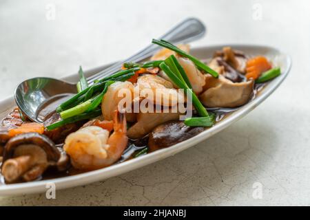 Gamberetti fritti, funghi Shiitake o funghi cinesi con salsa di ostriche in un bellissimo piatto ovale sul tavolo in pietra bianca, immagine ravvicinata Foto Stock