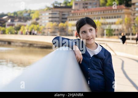 Bambina appoggiata su ringhiera con un look premuroso. Ritratto di bambino all'aperto Foto Stock