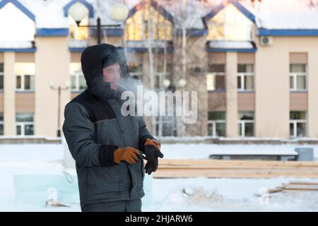 Ritratto di un costruttore sul posto di lavoro in una tuta invernale, con un cappuccio sulla testa Foto Stock