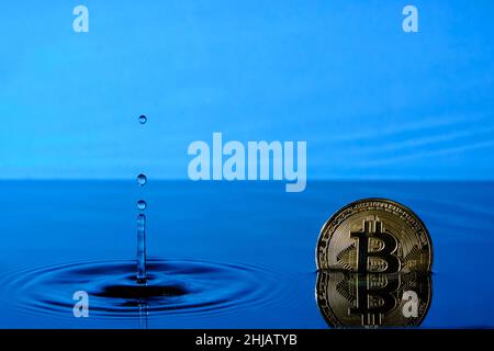 Spruzzi l'acqua da una pioggia che cade ed una moneta di bitcoin nell'acqua contro il cielo blu Foto Stock