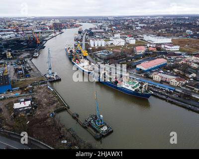 Gru industriali che sollevano container di carico contro il cielo blu vicino al mare nel porto di Kaliningrad, Russia. Vista dall'alto, vista aerea Foto Stock