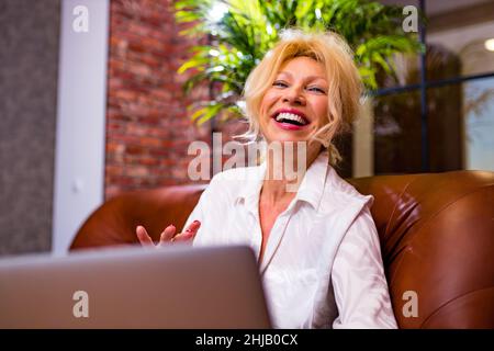 glamour donna designer di mezza età che completa un progetto di appartamento parlando con video chat con il cliente alla linea morta sera Foto Stock