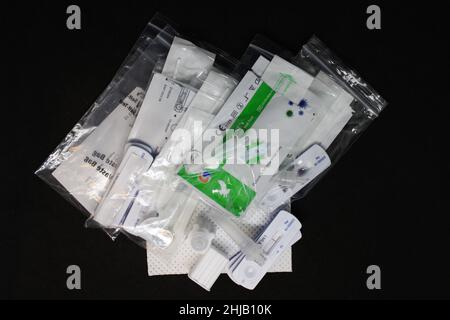 Pila di test a flusso laterale COVID-19 usati negativi in sacchetti di plastica con tamponi di plastica e provette di estrazione su sfondo nero Foto Stock
