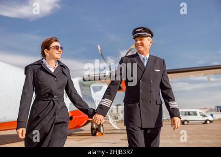 Gioioso pilota maschile e sua moglie si svegliano di mano in aeroporto Foto Stock