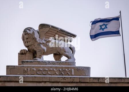 La bandiera israeliana sbatte mentre la neve copre la statua del leone alato in cima all'edificio generali in via Jaffa durante la nevicata del 27 gennaio 2022, a Gerusalemme, Israele. Gerusalemme è stata coperta dalla neve che ha raggiunto 10 - 20 centimetri (quattro - otto pollici) durante la notte. Foto Stock