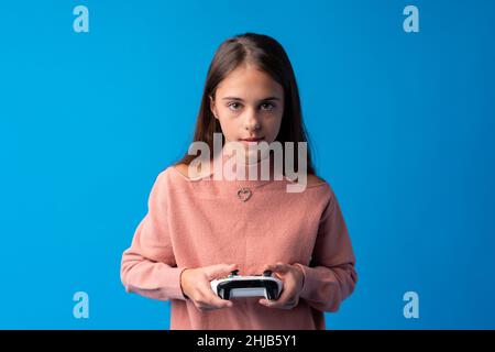 Giovane ragazza cute gioca gioco di computer con joystick su sfondo blu Foto Stock