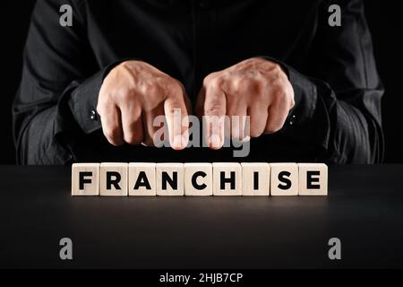 Mani maschili che puntano alla parola franchising su blocchi di legno. Concetto di modello di business. Foto Stock