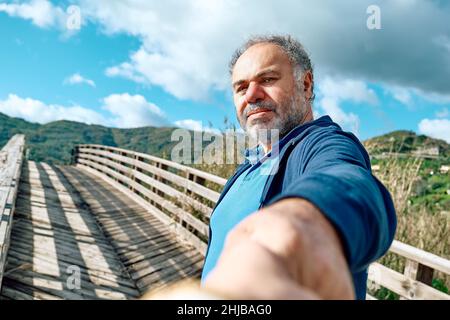 Seguimi. L'uomo tiene e tira la mano del fotografo e la guida su un ponte di legno nella natura rurale. Concetto di convivenza e spensieratezza moderna l Foto Stock